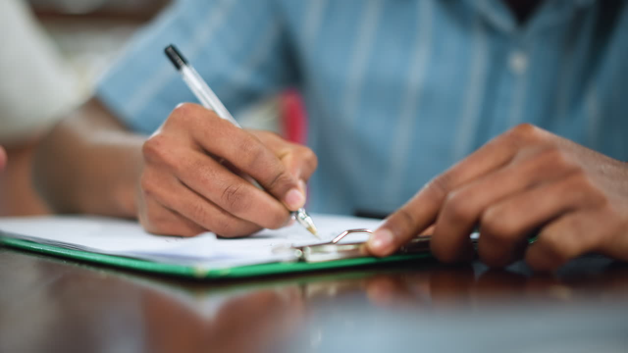 Front view of hand with firm grip on pen moving across white paper capturing textual creation under soft light focus highlighting purposeful pen motion and writing gesture conveying intent and craft