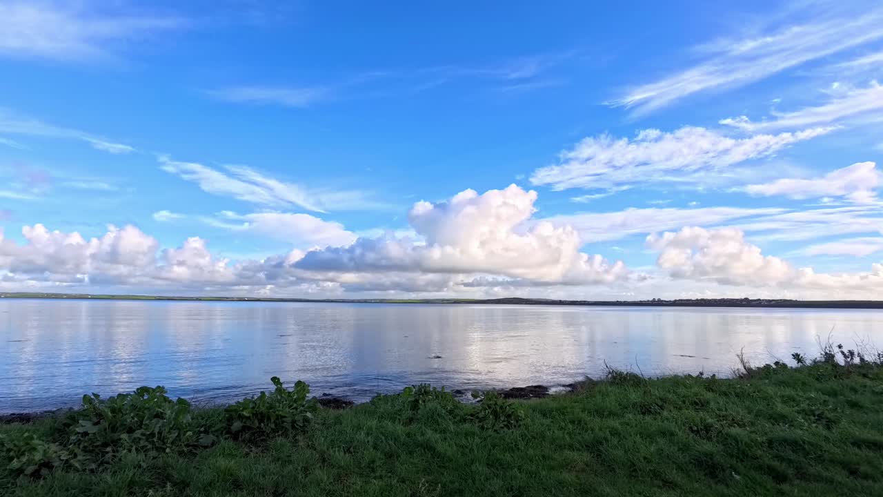 Reflection from time lapse clouds over changing sunlight on grassy Welsh coastal shoreline