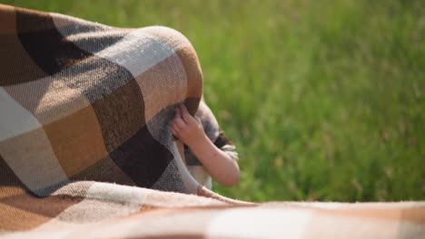 a young boy is playfully covered by a large plaid scarf in a grassy field. the child s hand peeks out from under the scarf, moment in the warmth of a sunny day surrounded by nature