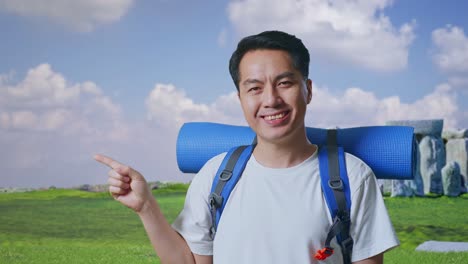 close up of asian male hiker with mountaineering backpack smiling and pointing to side while traveling in stonehenge