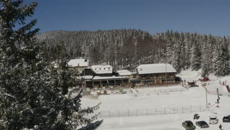 Complejo-De-Kope-En-Las-Montañas-De-Pohorje-Con-Gente-Jugando-En-La-Nieve,-Toma-Aérea-Revelada