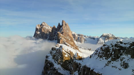 cinematic aerial orbit of snowy summit peaks of seceda mountain with fluffy clouds below