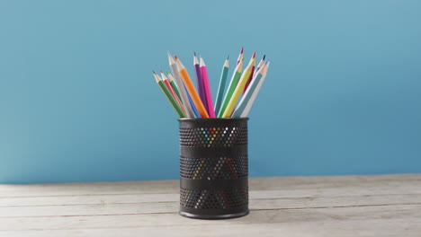 video of cup with crayons in wooden table over blue background