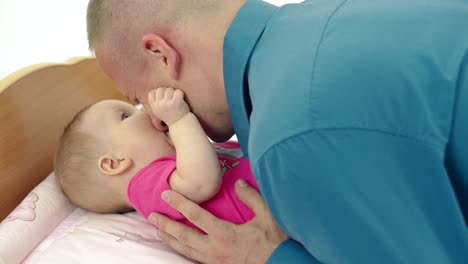 cu padre joven juega con pequeña hija dulce que se acuesta en una mesa de cambio él la besa se ríen