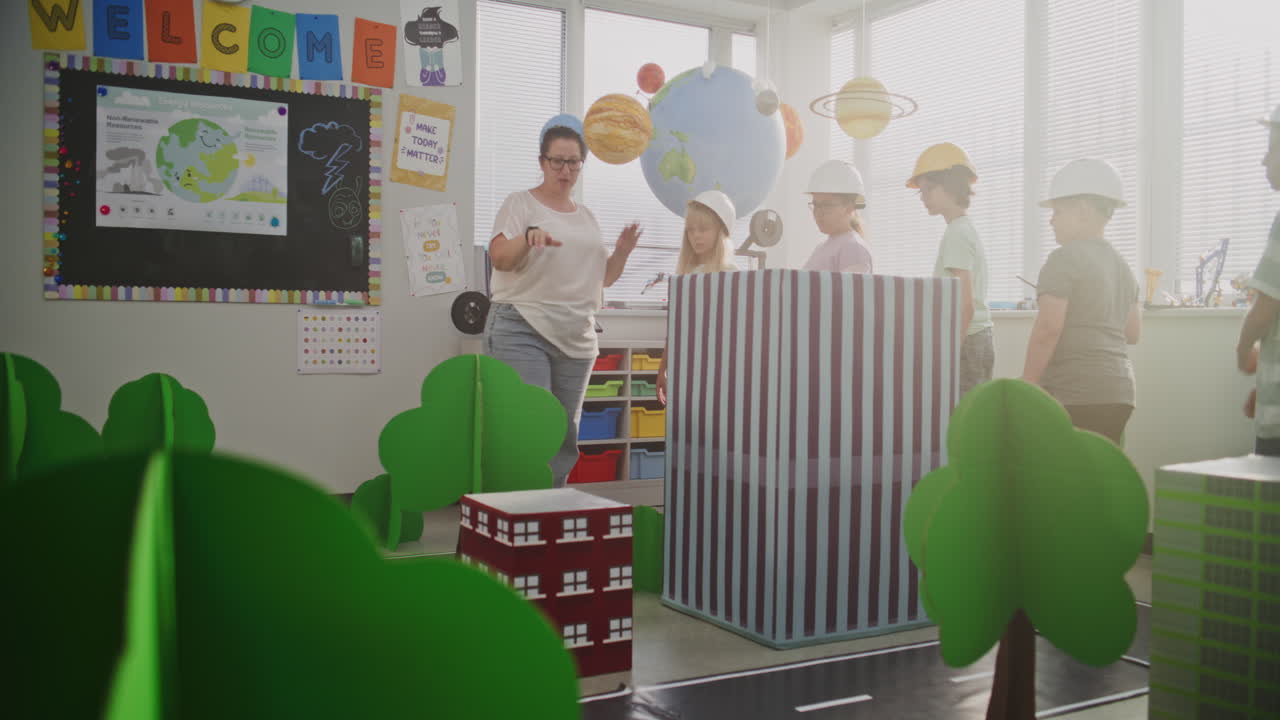 Female Teacher Guiding Elementary School Children in Classroom Activity with Cardboard Urban
