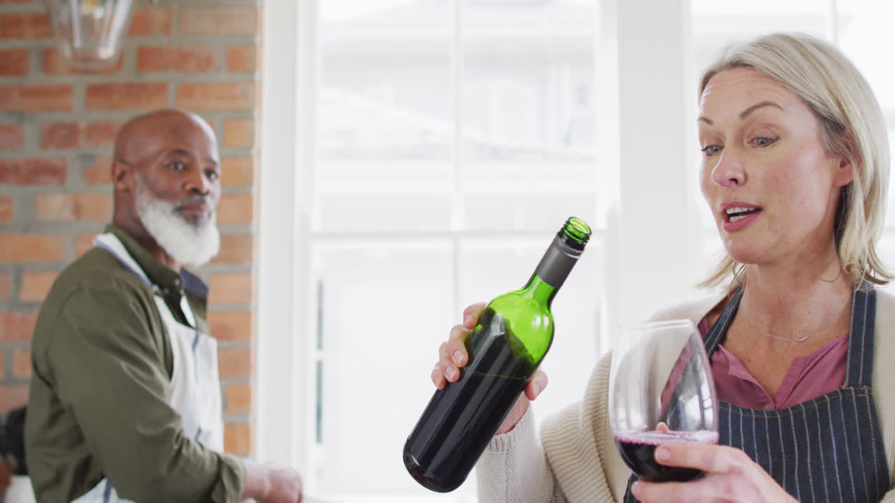 코카시안 고위 여성이 집에서 부에서 컵에 와인을 고 있습니다.