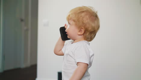 little boy in white t-shirt walks holding phone about room