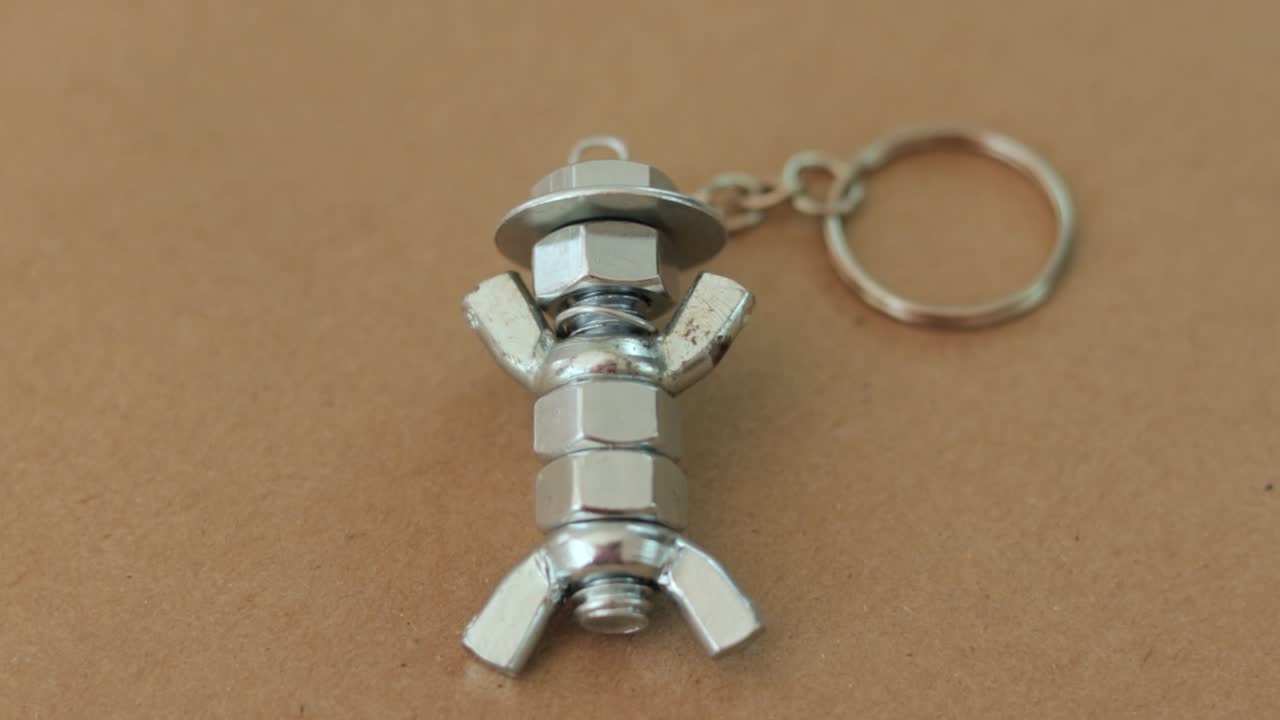 모자를 입은 인물과 비슷하게 만들어진 은색 키체인, 견과류와 볼트로 만들어진