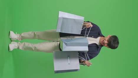 vista completa de un hombre de compras asiático siendo feliz después de abrir la bolsa de compras mientras está de pie frente a la pantalla verde