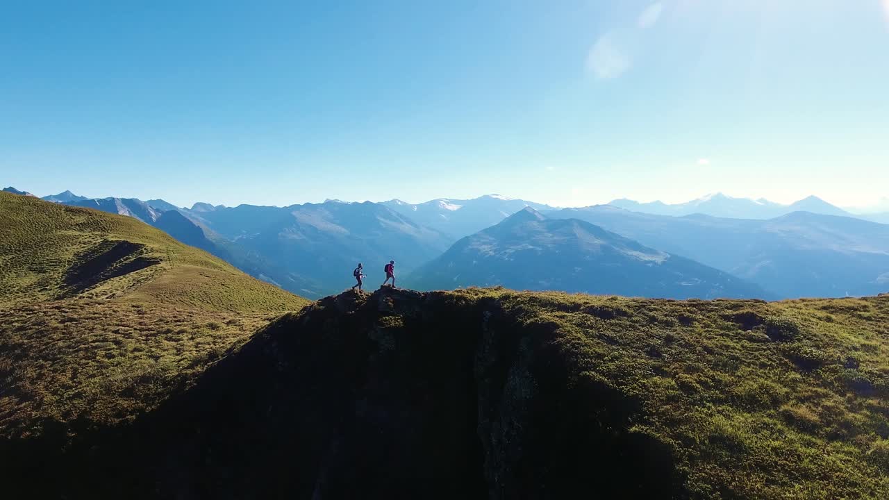 Epic aerial drone shot of two people hiking along an Alpine mountain ridge with a stunning mountain landscape in the background. Hiker couple on a summer adventure in the Austrian Alps.