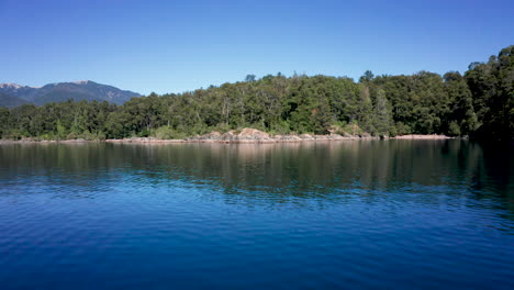 aerial rising from blue lake over green hilly forest in argentina