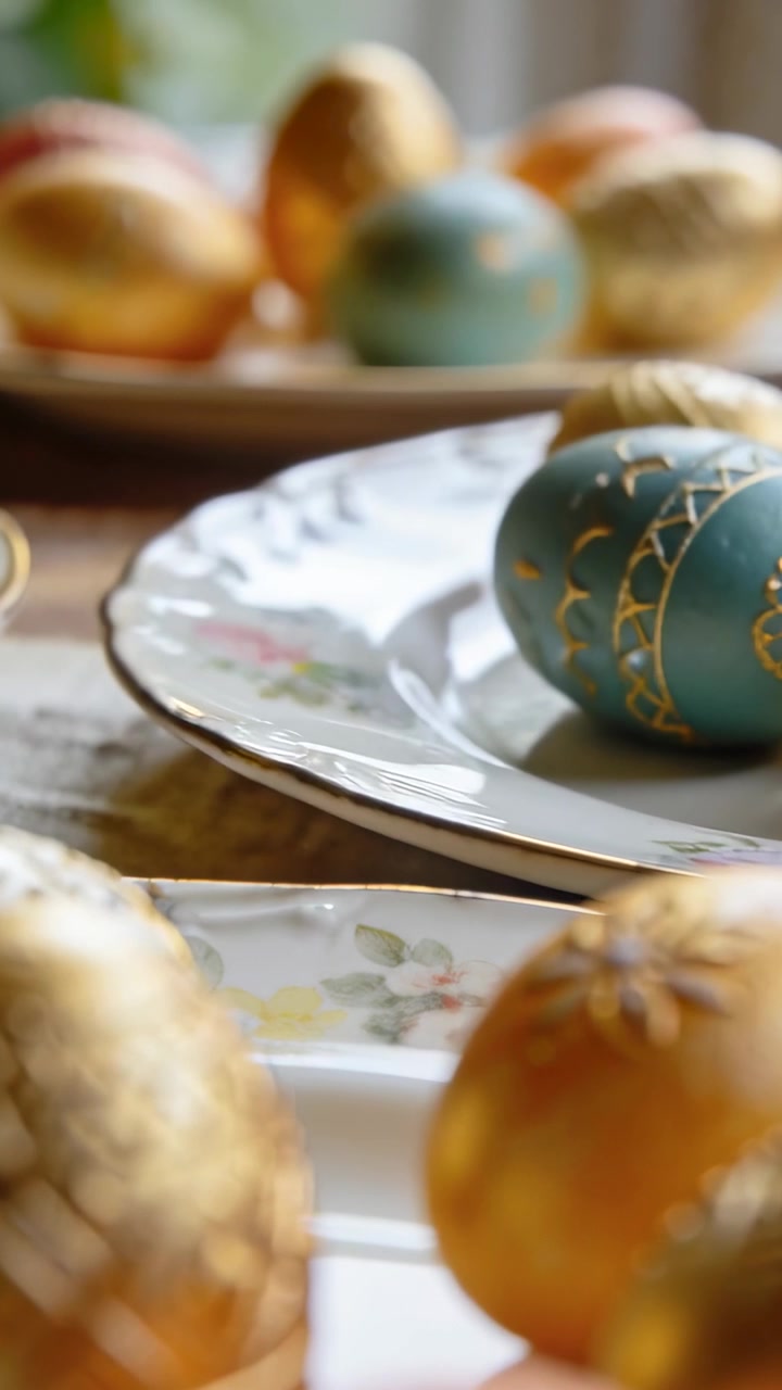 Panning cluster of gold and teal eggs on table near window, revealing floral china plates