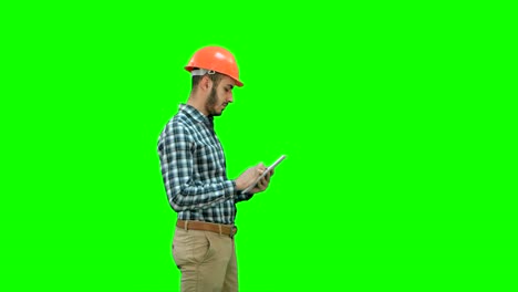 contractor engineer in hardhat inspecting construction site holding digital tablet on a green screen, chroma key