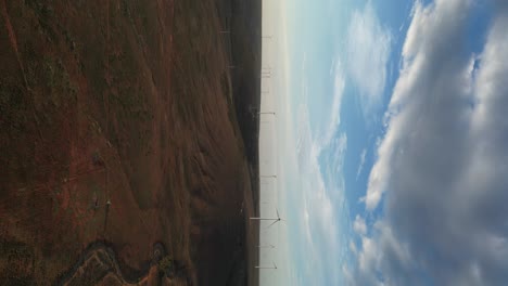 Vertical-drone-shot-showing-windfarm-with-windmills-on-sandy-and-rocky-landscape-of-Australia-during-sunset-time