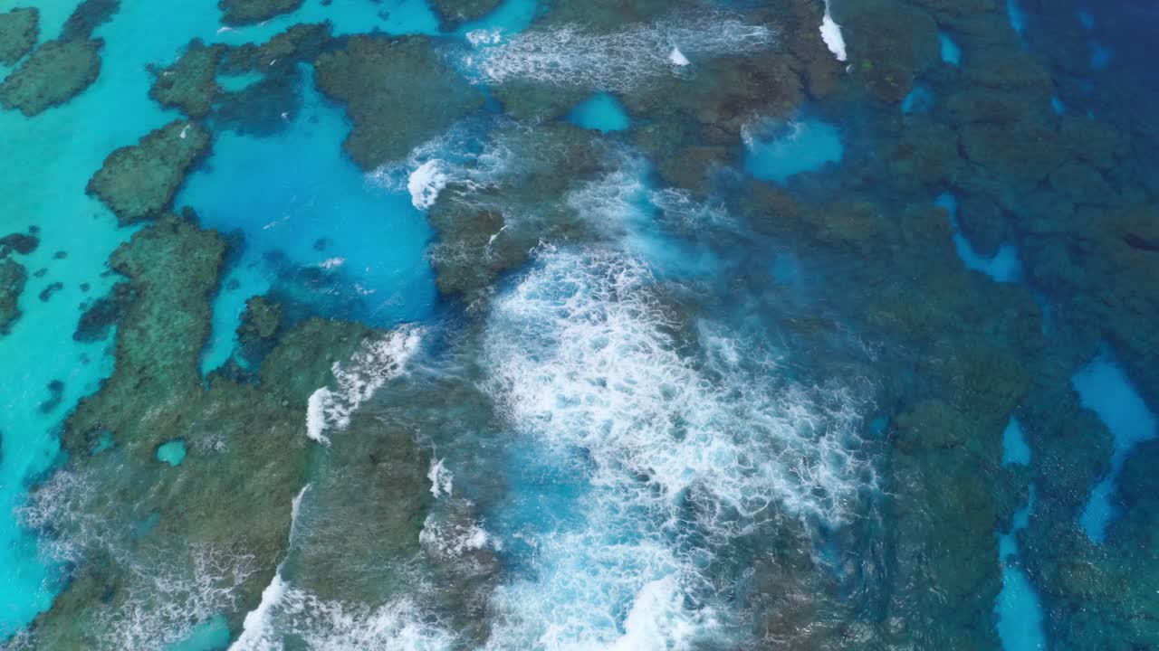 un dron captura la belleza de un arrecife de laguna azul con olas que rompen durante el día, mostrando los colores vibrantes y el movimiento dinámico del agua