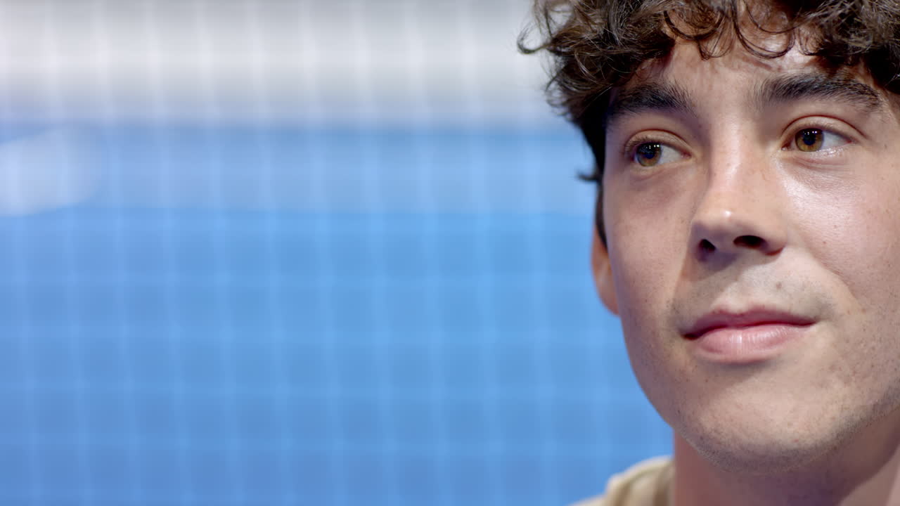 Young man smiling confidently on padel tennis indoor court with net in background, copy space