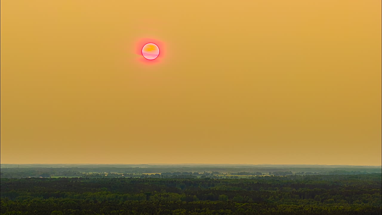 Drone hyperlapse of pink sun glowing over hazy evening forest horizon at sunset