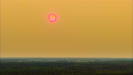 drone hyperlapse of pink sun glowing over hazy evening forest horizon at sunset