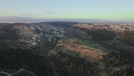 the mountainous area of ramot neighborhood in jerusalem, israel on the right and beit iksa, the palestinian village on the left over the kidron valley, israel - drone sliding shot