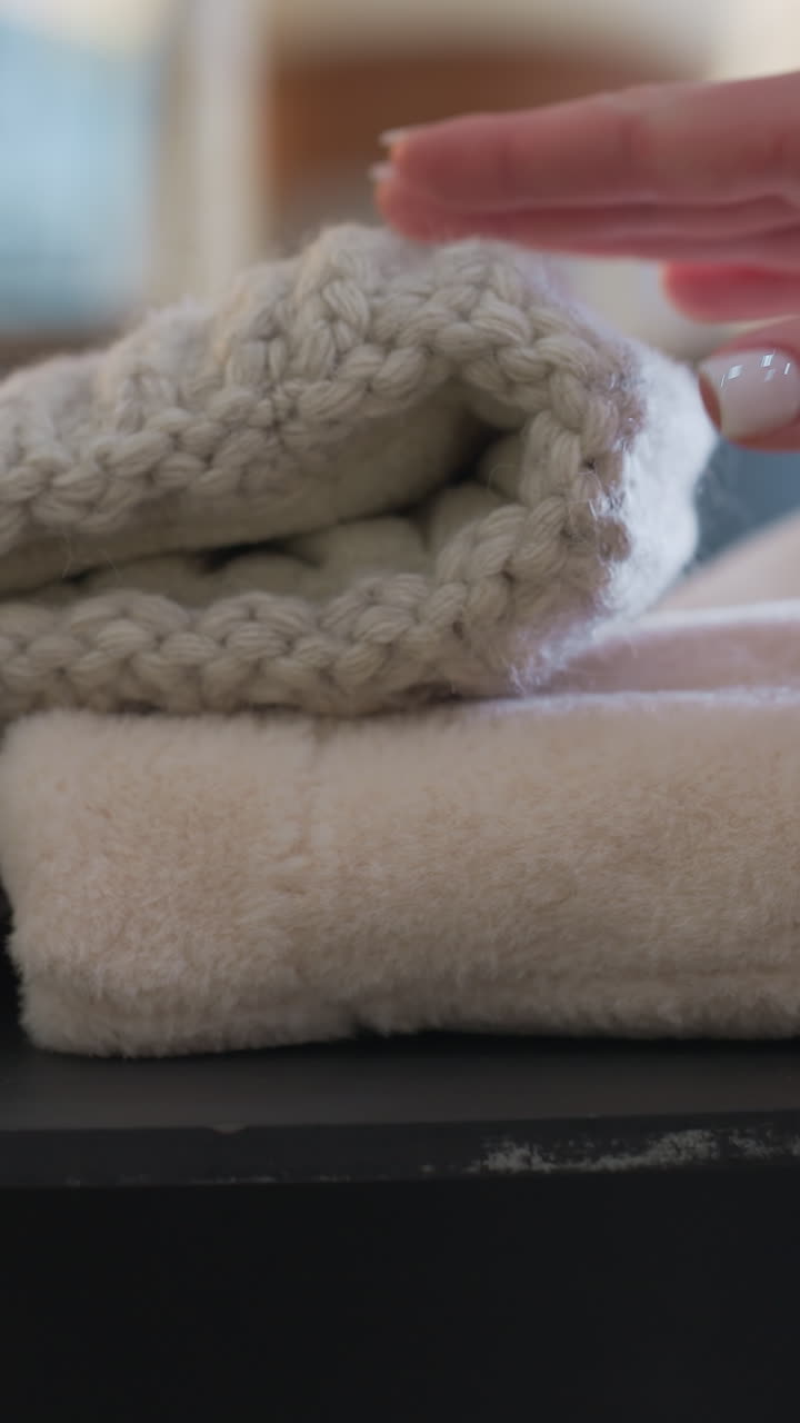 Close-up of a person hand reaching for a knitted head warmer placed on a soft fluffy fabric, cozy winter accessories with blurred background and warm tones