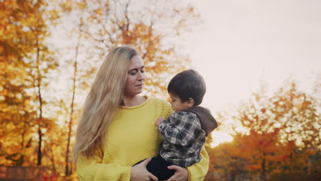 Mom-carries-a-baby-in-her-arms,-walks-through-a-beautiful-park-at-sunset