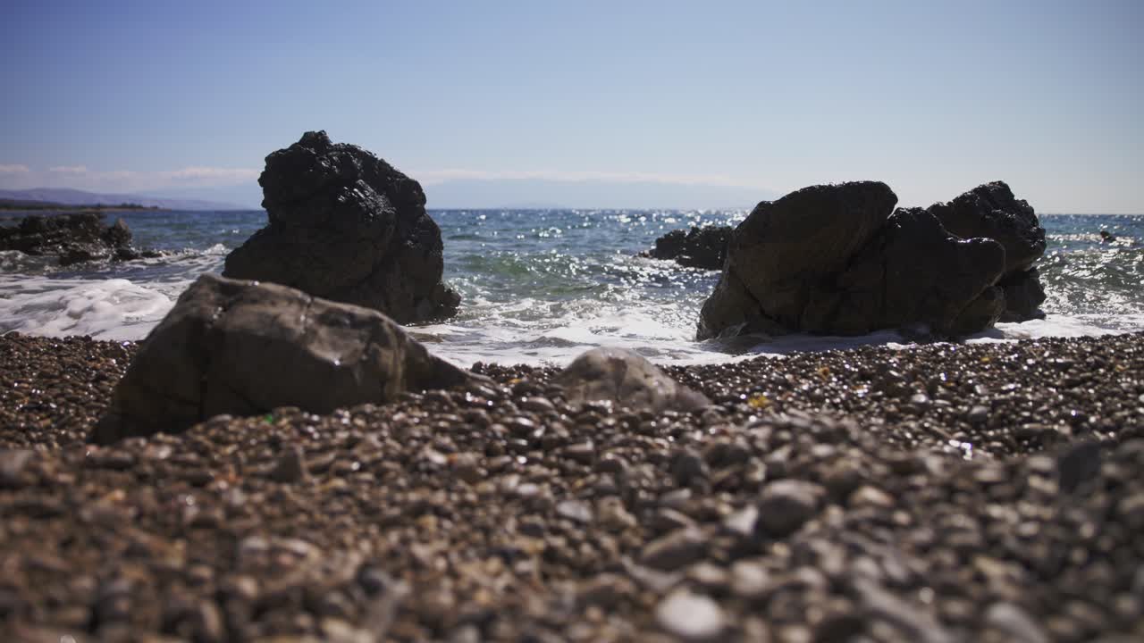 Bølgerne rammer klipperne på rullestensstranden - slowmotion.