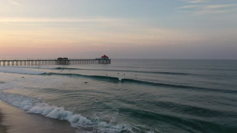 in 4k a surfer catches a wave at sunrise in surf city california usa with the pier beautifully displayed in the background