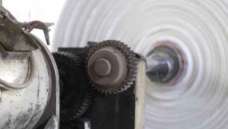 close up of two machine cogs turning machine roller at plastic bag factory