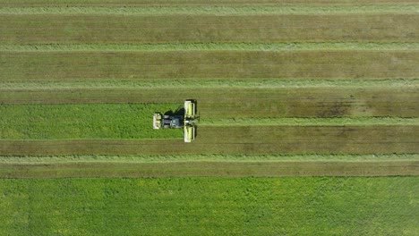 Aerial-establishing-view-of-a-tractor-mowing-a-fresh-green-grass-field,-a-farmer-in-a-modern-tractor-preparing-food-for-farm-animals,-sunny-summer-day,-ascending-birdseye-drone-dolly-shot-moving-left