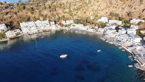 vista de drones en grecia volando sobre el mar azul en loutro pequeña ciudad de casas blancas y pequeños barcos al lado de una colina en un día soleado