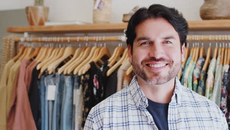 retrato del propietario masculino de una tienda de moda de pie frente a la ropa en los rieles
