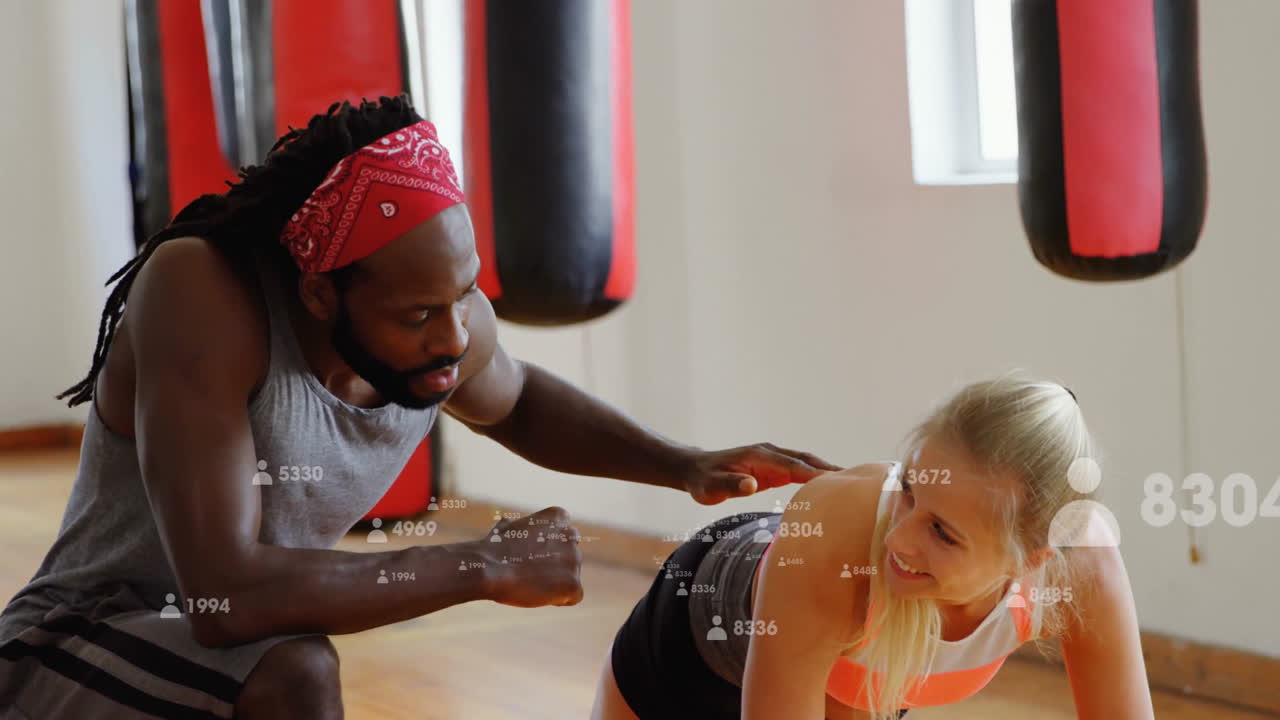 male trainer kneeling coaching female trainee performing plank in gym with floating metrics