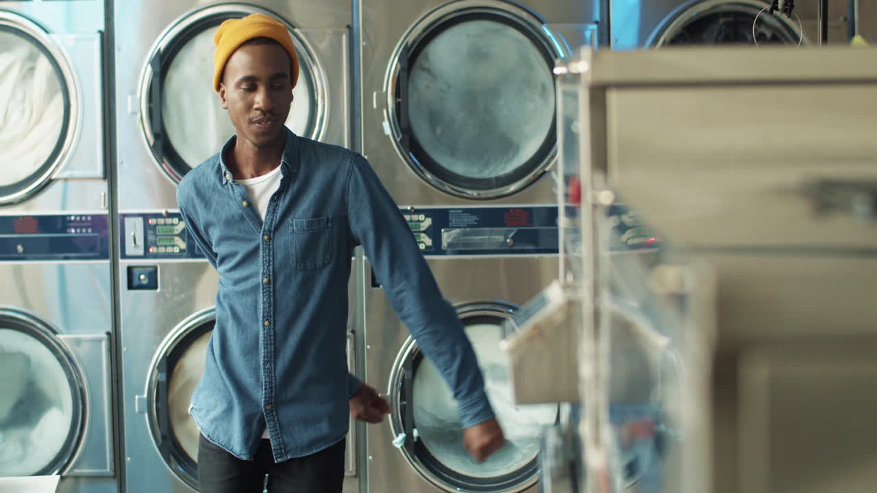 기계가 배경에서 세탁하는 동안 세탁 서비스 룸에서 재미와 춤을 추는 젊은 세련된 쾌활한 남자