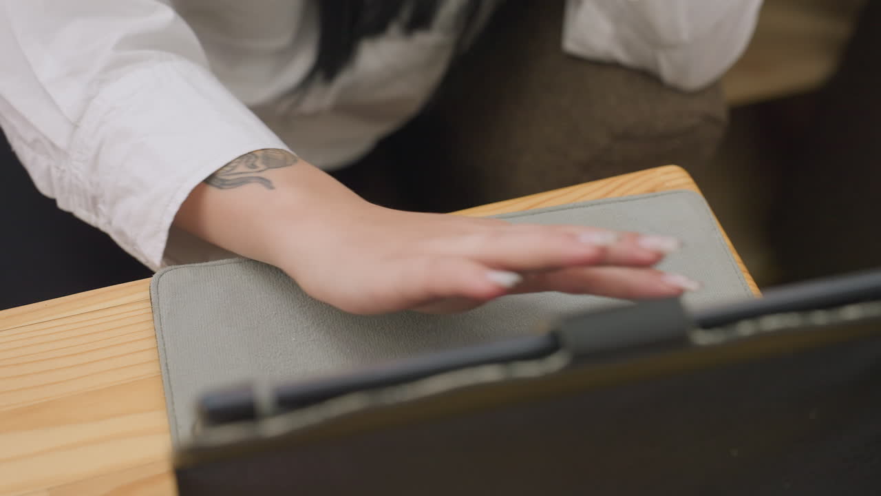 female hand with polished nails and wrist tattoo gently sliding across tablet surface during relaxed browsing session in cozy cafe setting with wooden table and soft indoor light ambiance