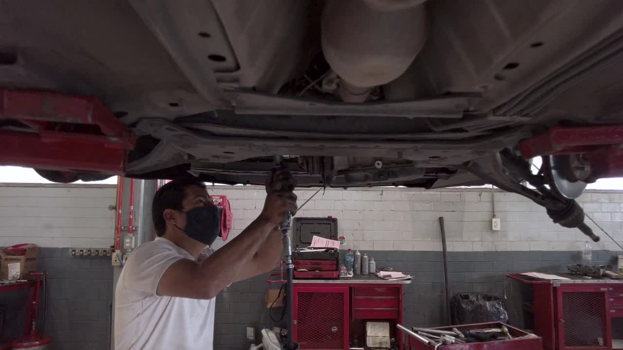 Latin male mechanic technician repairing the engine from the bottom of a car at a workshop station garage at mexico latin-america
