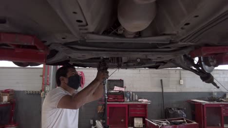 latin male mechanic technician repairing the engine from the bottom of a car at a workshop station garage at mexico latin-america