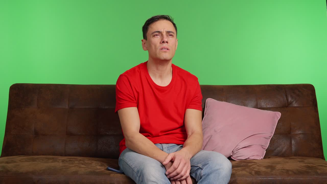 Sad man sitting on sofa, waiting for message on green screen