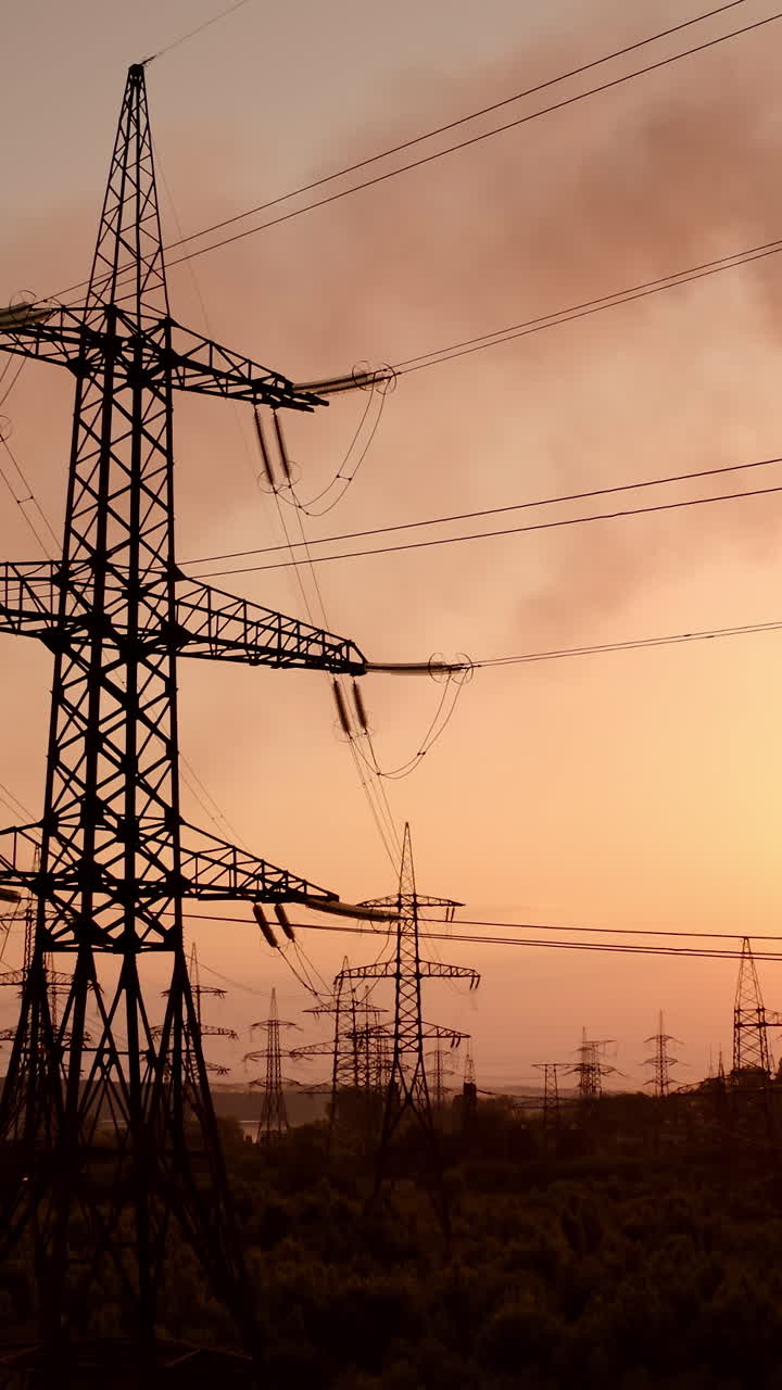 Power station at dusk. Transmission lines near smoke pipes from industrial plant. Chemical emissions in the air from industry. Electric towers with wires at sunset. Vertical video