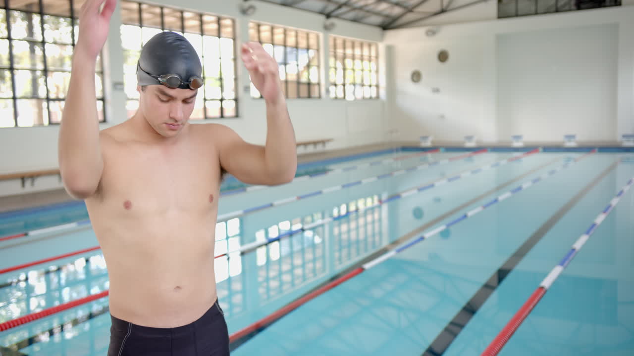 Male Swimmer in swim cap standing by indoor pool, preparing for practice, copy space