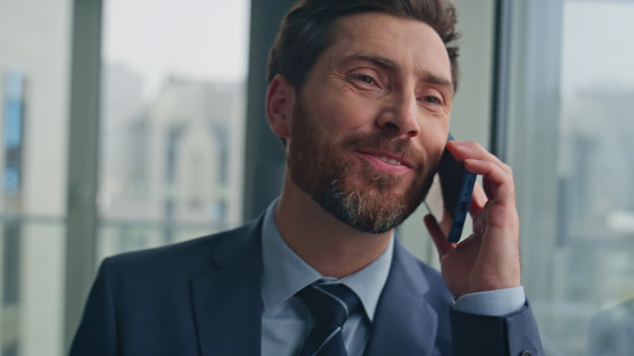 Overjoyed boss speaking mobile phone at big windows cabinet closeup. Man call