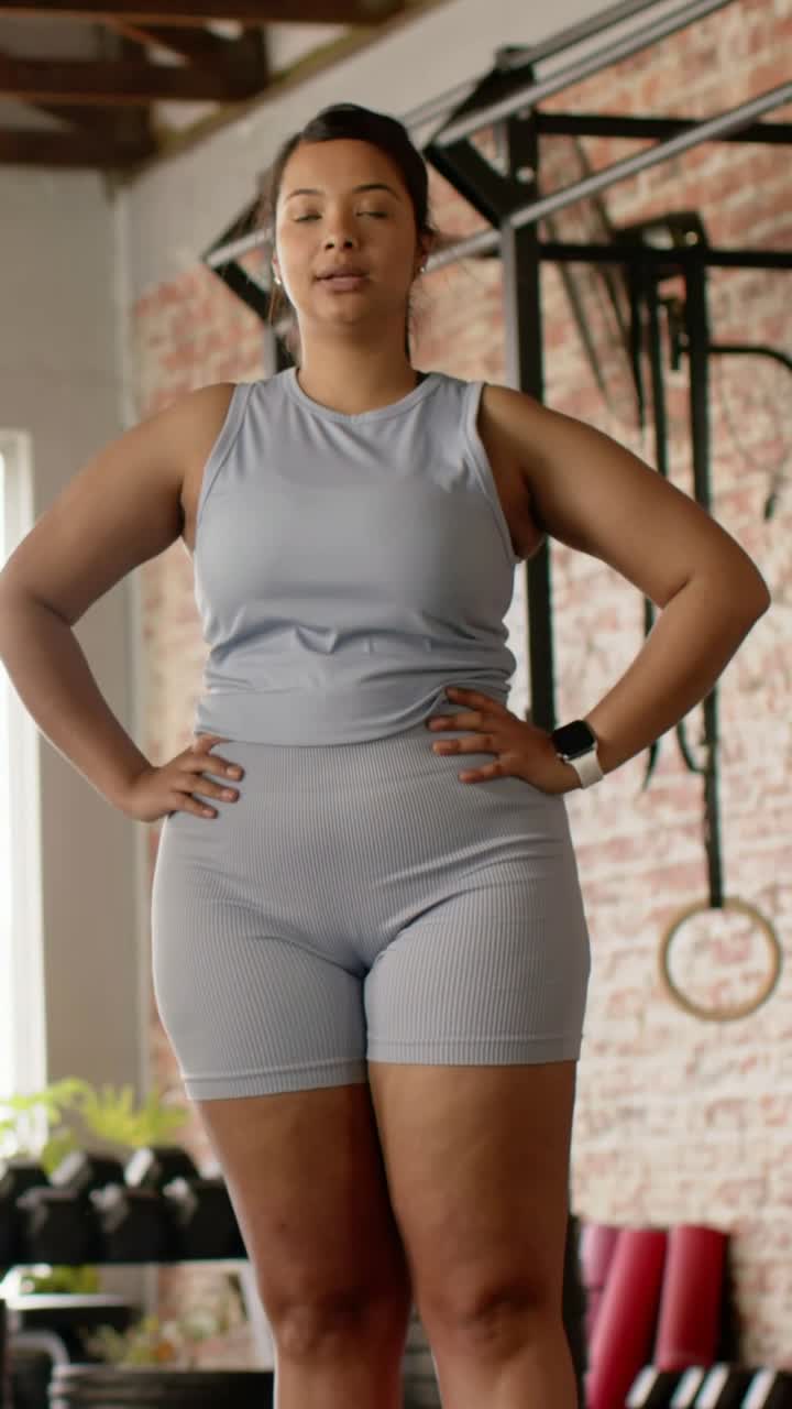 Video verticale: Donna con top senza maniche e pantaloncini che espira, sollevando un ginocchio per l'equilibrio vicino a un'attrezzatura.