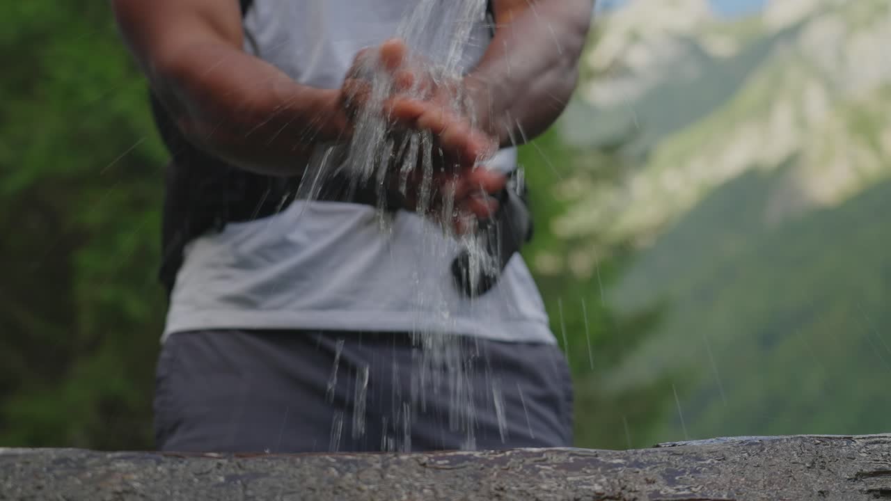 Man washes hands in flowing water while hiking in the mountains on a sunny day