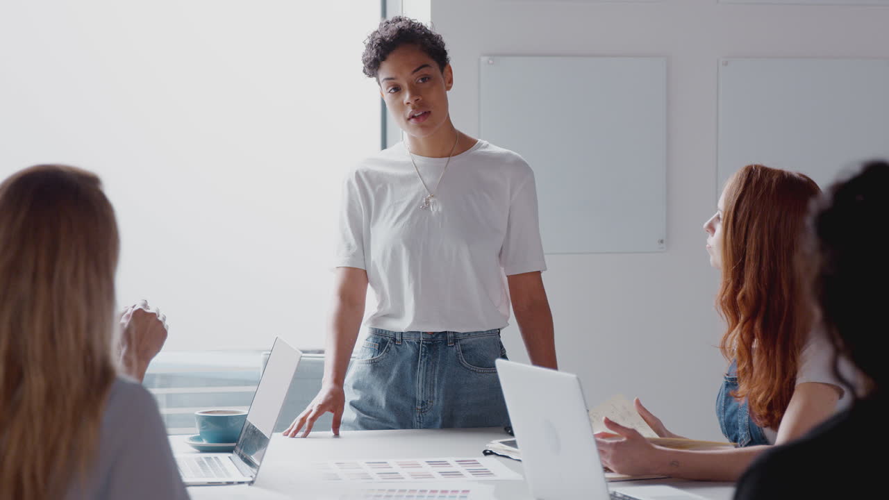 jefa da una presentación a un equipo de jóvenes mujeres de negocios que se reúnen alrededor de una mesa en una oficina moderna