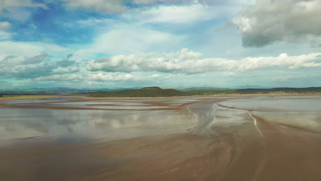 Aerial-landscape-over-a-coastal-bay-at-low-tide,-showing-the-natural-pattens-in-the-golden-sand,-bright-sunny-day