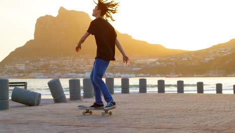 Side-view-of-young-caucasian-man-practicing-with-skateboard-on-beach-promenade-during-sunset-4k