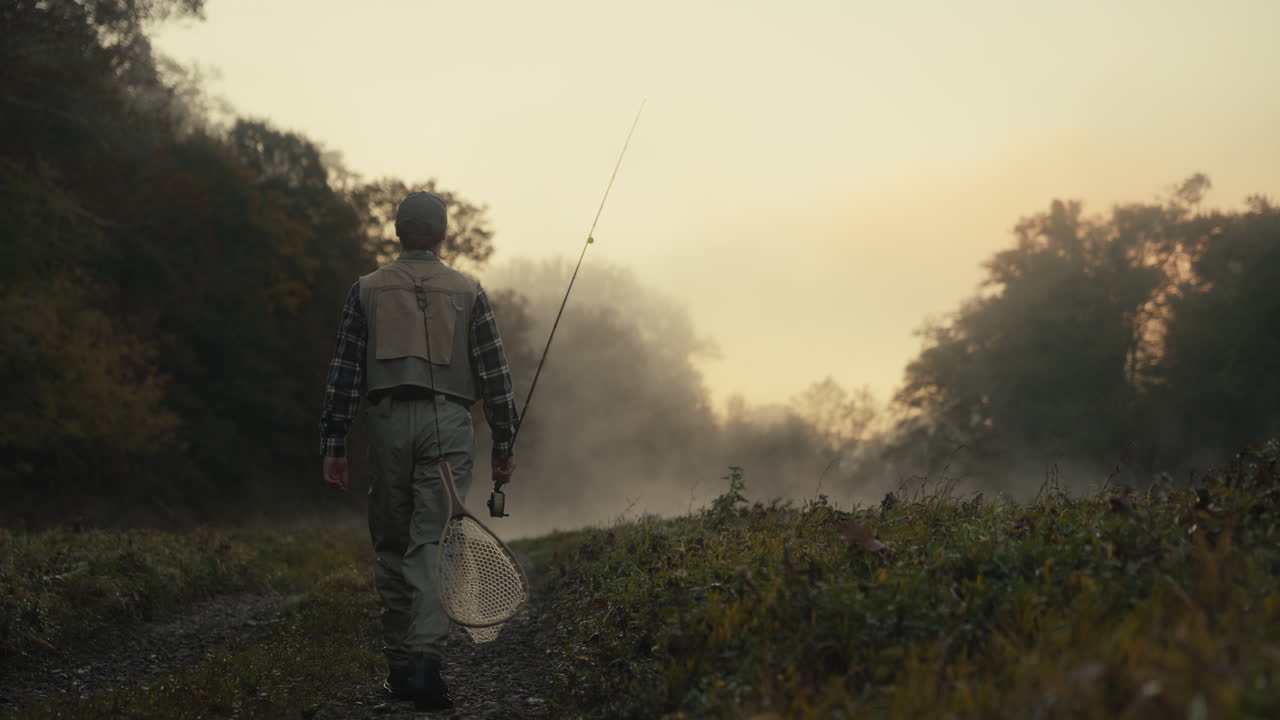 Fisherman walking a trail in a foggy forest at sunrise
