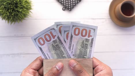 manos sosteniendo un sobre con nosotros billetes de cien dólares