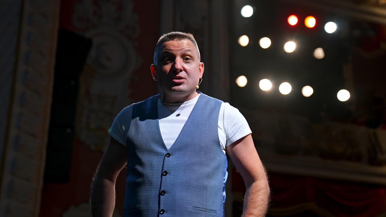 Man in suit speaking jokes in micropphone standing on stage. Funny performance. Comedian in good humor speaks to the audience.