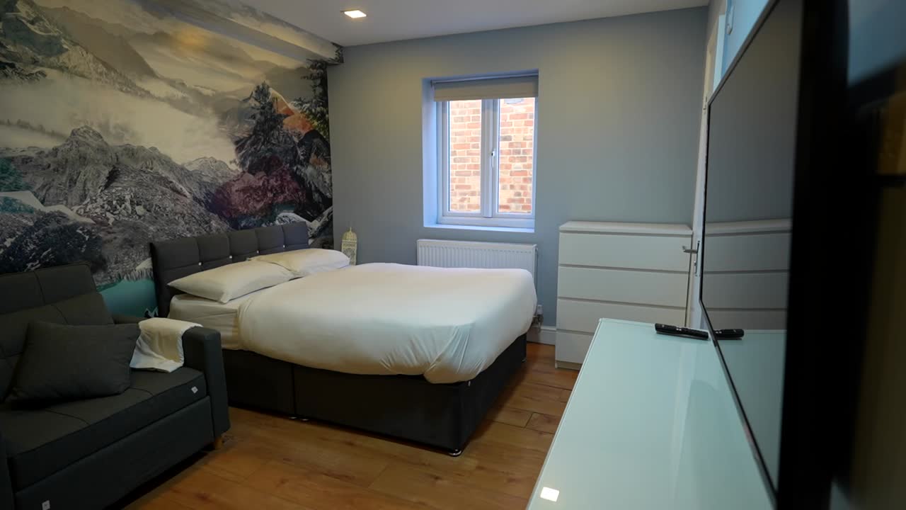 Modern hotel room with a king bed, sofa, and mountain mural on the wall