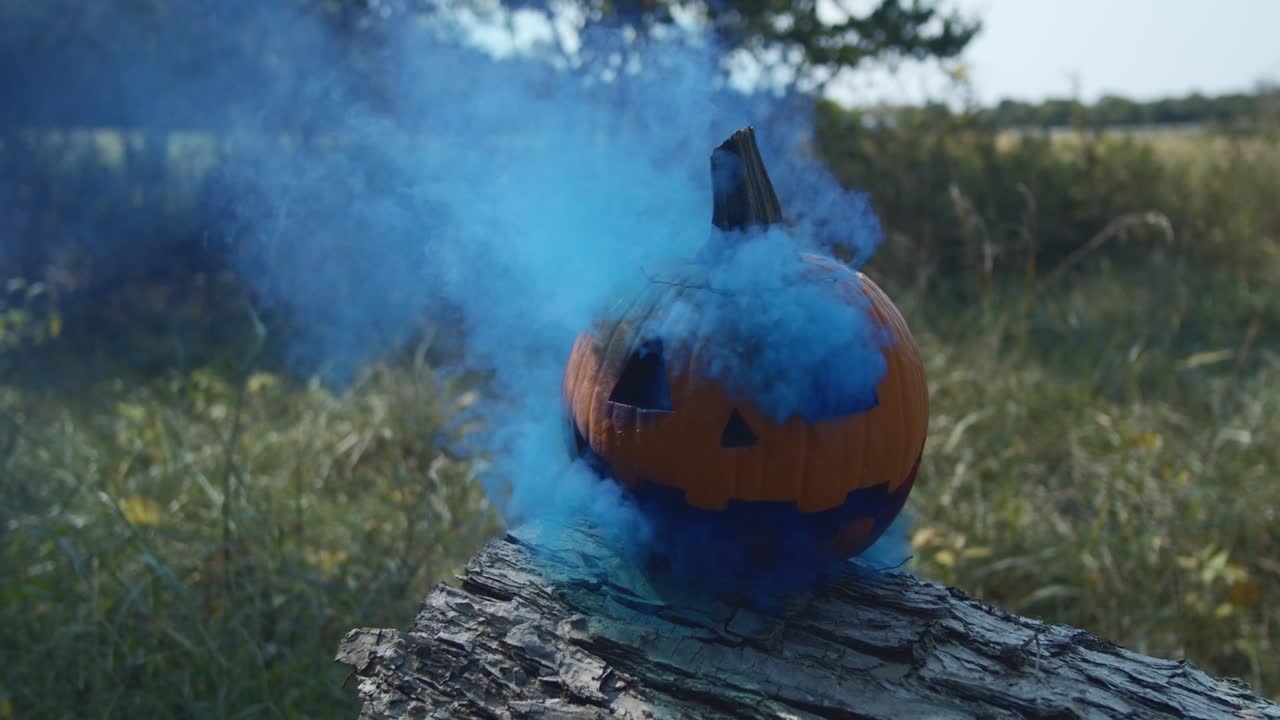 A Halloween pumpkin emitting eerie blue smoke, set outdoors during the day in a natural environment, creating a spooky yet whimsical atmosphere.